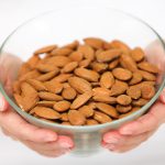 Almonds nuts - woman showing raw almond bowl close up. Healthy food concept in studio with hands lifting bowl of unprocessed almonds isolated on white background.