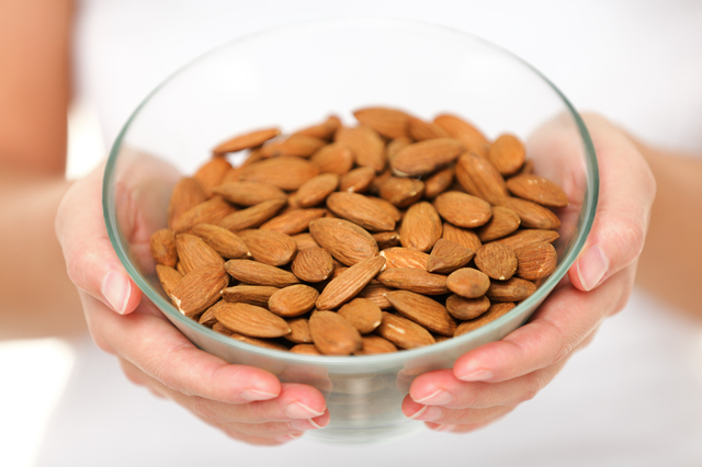 Almonds nuts - woman showing raw almond bowl close up. Healthy food concept in studio with hands lifting bowl of unprocessed almonds isolated on white background.